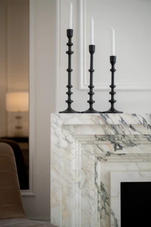 Three black candlestick holders with white candles are displayed on a marble fireplace mantel in a bright, modern home interior.
