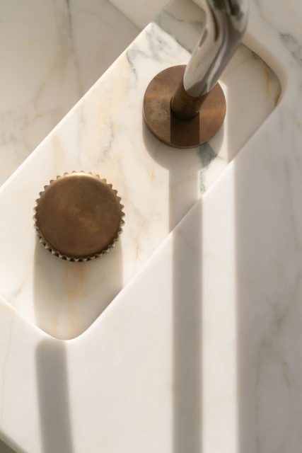 Elevated view of a bathroom sink made of white marble, featuring a metallic faucet and a brass-colored drain cover.