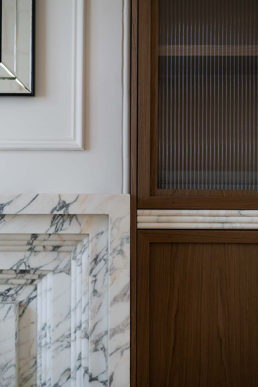 Interior design featuring a brown wooden cabinet with fluted glass, set against a white wall with marble fireplace surround.