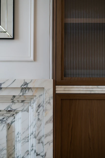 Interior design featuring a brown wooden cabinet with fluted glass, set against a white wall with marble fireplace surround.