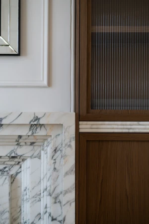 Interior design featuring a brown wooden cabinet with fluted glass, set against a white wall with marble fireplace surround.
