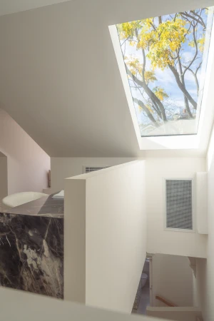 Interior view of a modern home features a window view of a tree with yellow leaves. The room is painted in white with marble details.