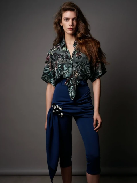 Fashionable woman in floral shirt and capri pants poses in a studio, showcasing contemporary style and apparel in portrait.