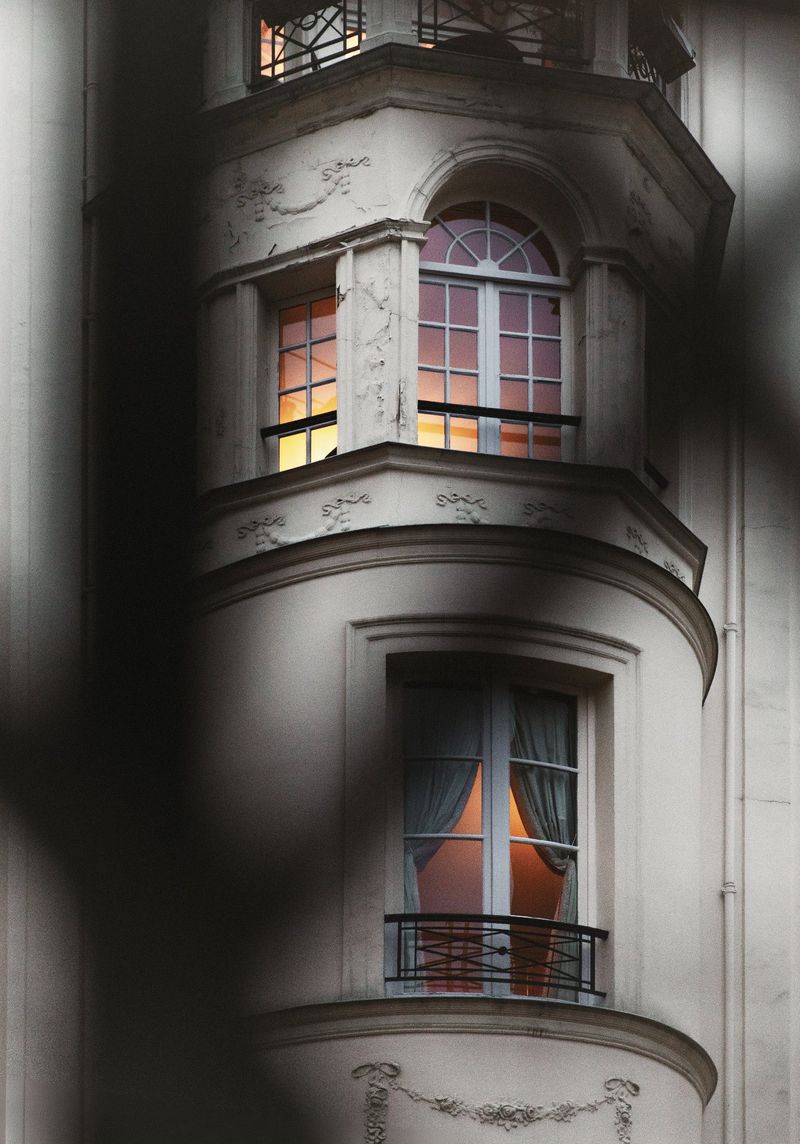 Exterior shot of a white building with rounded corners and windows, featuring classical architectural details and warm light inside.
