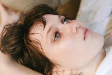 Close-up portrait of a woman with brown hair lying down, looking upward with a candid expression.