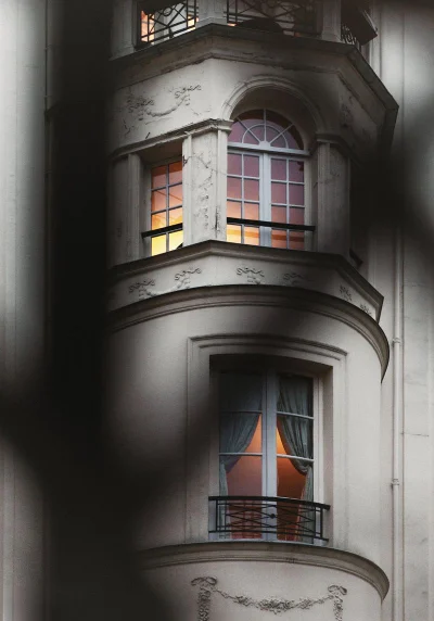 Architectural view of a classic curved building facade with lighted windows behind dark foreground silhouettes