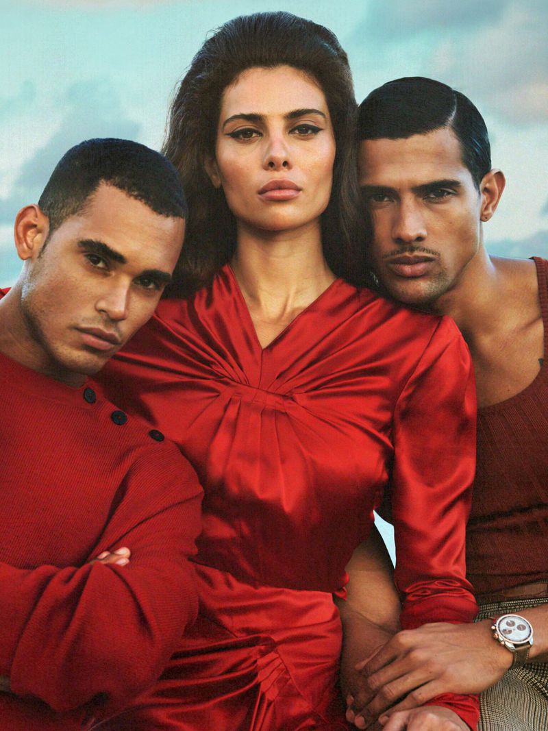 Portrait of a woman in red dress with two adult males; indoor studio setting with soft lighting and a vintage fashion editorial style.