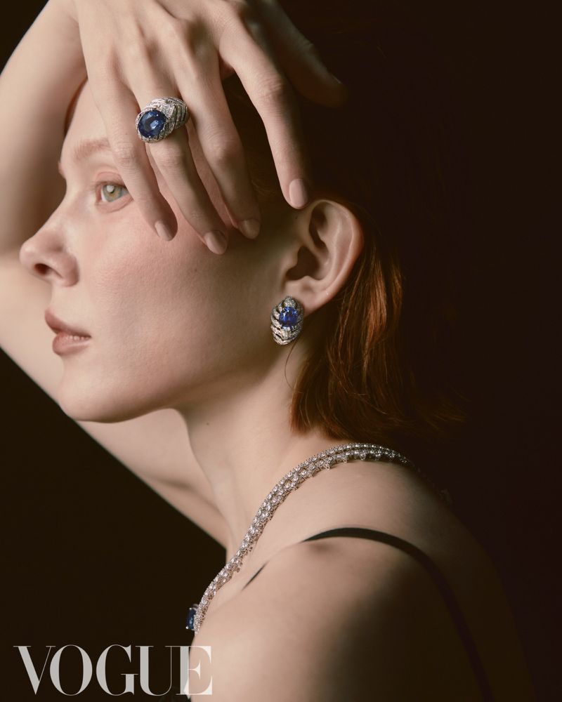 Elegant woman with jewelry: a close-up of a red-haired female model wearing statement diamond earrings, necklace, and ring against a dark background.