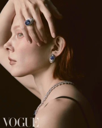 Elegant woman with jewelry: a close-up of a red-haired female model wearing statement diamond earrings, necklace, and ring against a dark background.