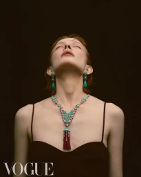 Model with head tilted back wearing green drop earrings and an elaborate beaded necklace against a dark background for Vogue Taiwan.