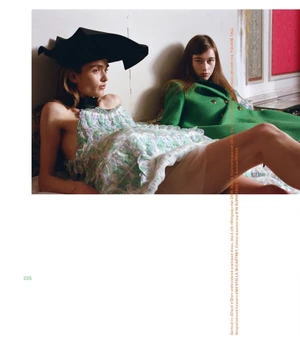 Two female models posing indoors, one wearing a sculptural black hat and patterned dress, the other in a green coat