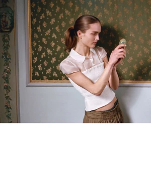 A woman holding a small decorated egg in front of green patterned wallpaper