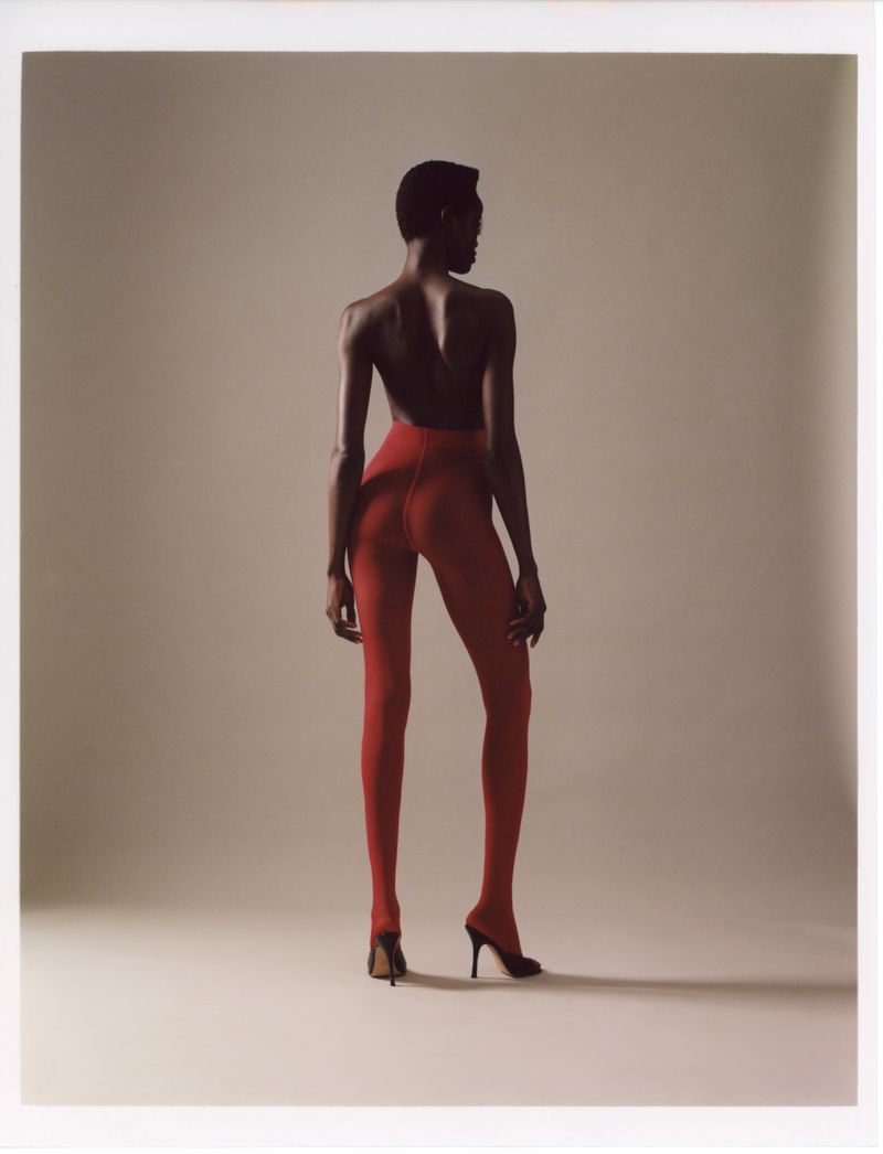 Model Anyiel Majok from behind wearing red tights and black heels against a neutral studio background