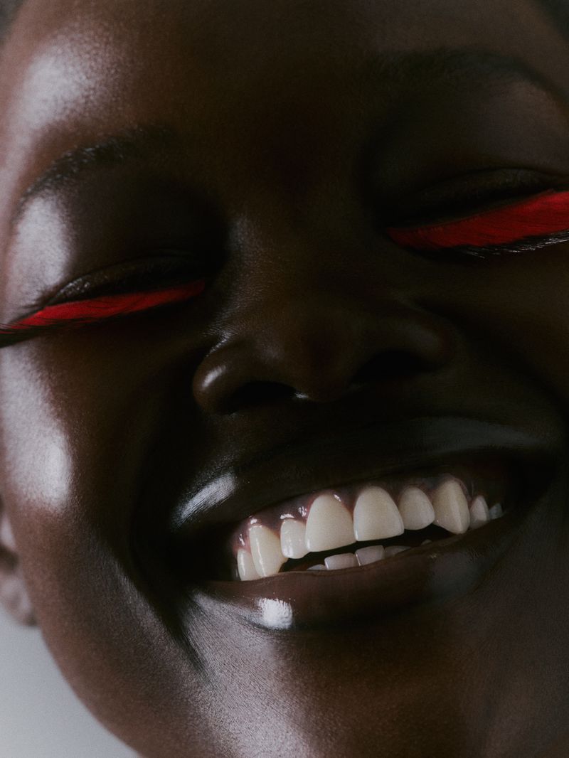 Close-up portrait of a smiling, dark-skinned woman with red eyeliner, showcasing dental aesthetics and makeup artistry in a studio setting.