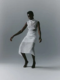 Model Anyiel Majok in a white semi-sheer dress against a grey seamless background for Mia Le Journal.