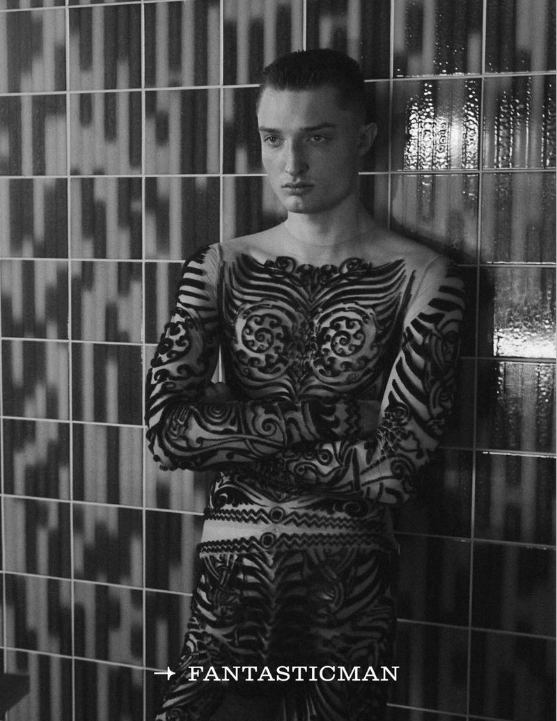 Monochrome portrait of a fair-skinned adult male fashion model with a serious expression, wearing body art or fitted patterned clothing.