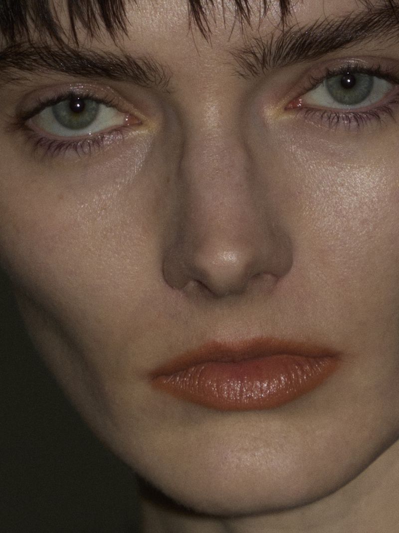 Close-up portrait of a young adult woman with fair skin, light blue eyes, and auburn-tinted lips, looking directly at the camera.