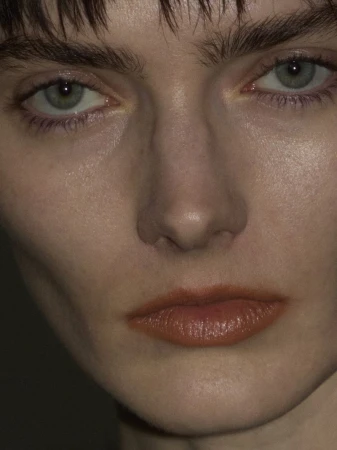 Close-up portrait of a young adult woman with fair skin, light blue eyes, and auburn-tinted lips, looking directly at the camera.