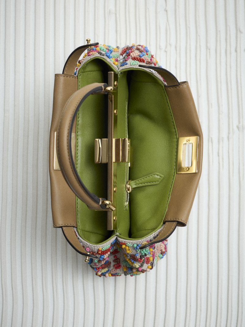 Overhead shot of an open handbag with a tan leather exterior, colorful beaded accents, gold hardware, and a green leather interior.