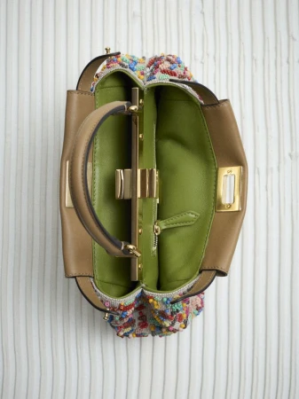 Overhead shot of an open handbag with a tan leather exterior, colorful beaded accents, gold hardware, and a green leather interior.