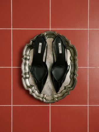 Black slingback heels on a decorative silver tray against a textured red tiled surface. Fashionable footwear still life.