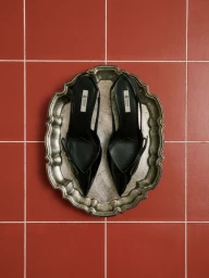 Overhead shot of a pair of black slingback heels resting on an ornate silver tray against a red tiled surface.