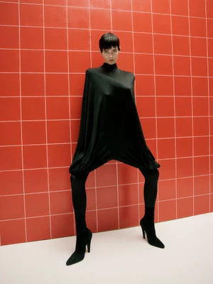 Model in black draped outfit and boots standing against a red tiled wall for Love Want Magazine Outsiders