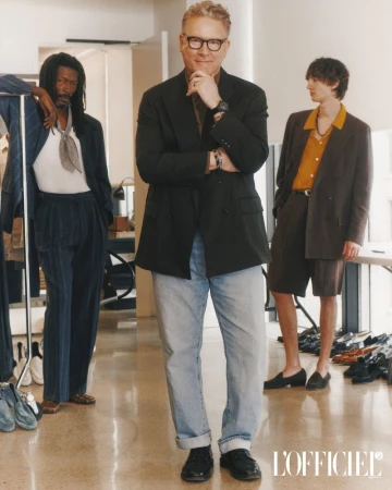 Three men in stylish blazers pose indoors; one middle-aged with glasses and two young adults. Men's fashion, indoor, neutral lighting.