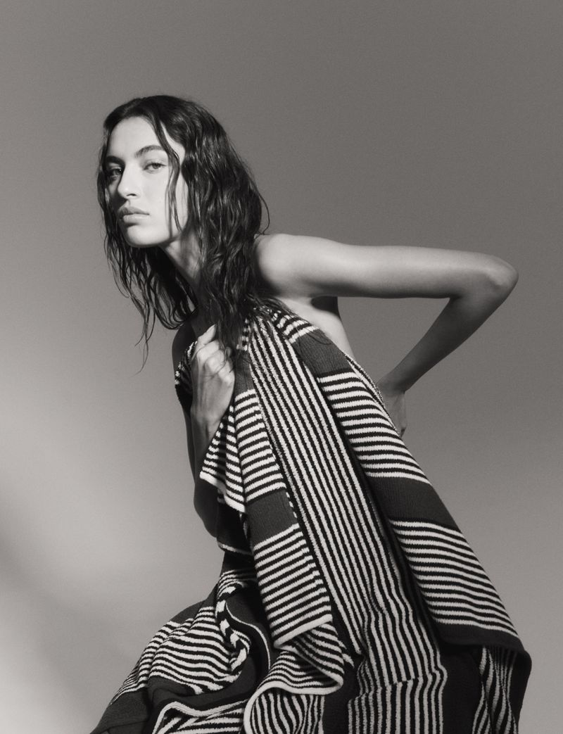 Striking black and white portrait of a woman draped in a striped fabric, gazing intensely at the camera in a studio setting.
