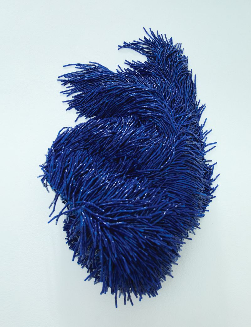 Abstract art piece featuring a dense cluster of blue bristled elements arranged in a swirling, organic shape against a bright white backdrop.