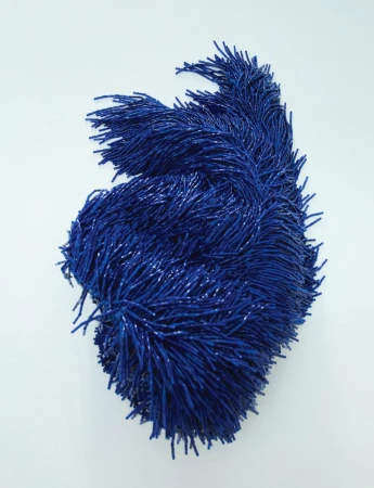 Abstract art piece featuring a dense cluster of blue bristled elements arranged in a swirling, organic shape against a bright white backdrop.