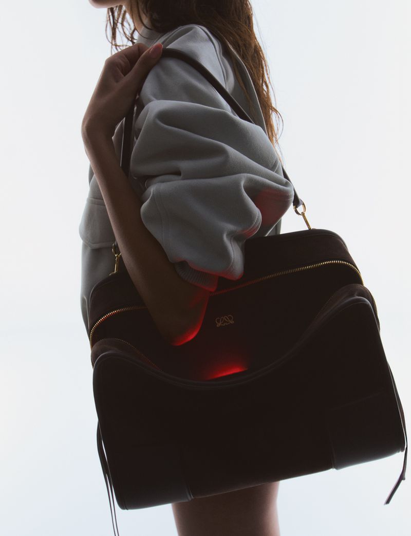Fashion shot of a woman with long hair wearing a gray sweatshirt and carrying a large, dark brown leather handbag over her shoulder.
