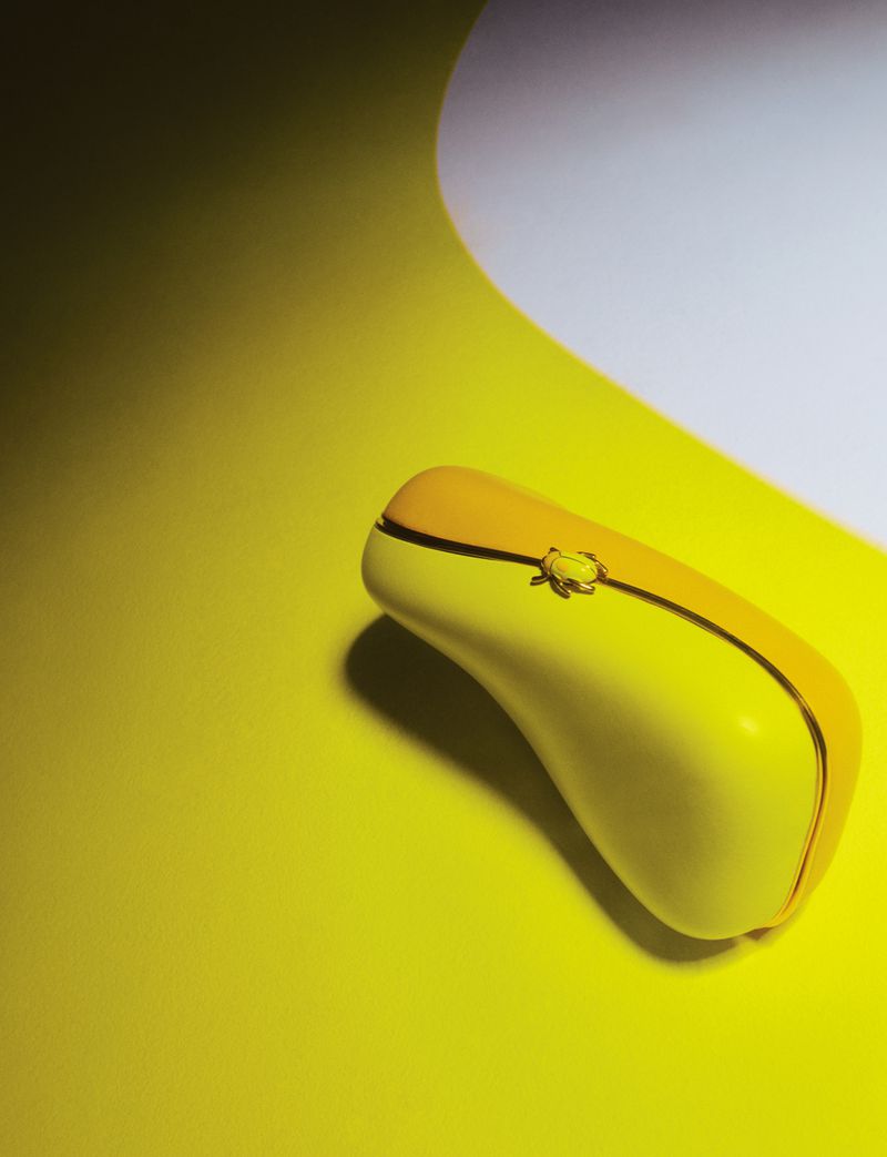 Elevated shot of a yellow wireless computer mouse with a black accent stripe on a yellow surface with white gradient background.