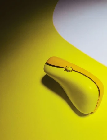 Elevated shot of a yellow wireless computer mouse with a black accent stripe on a yellow surface with white gradient background.