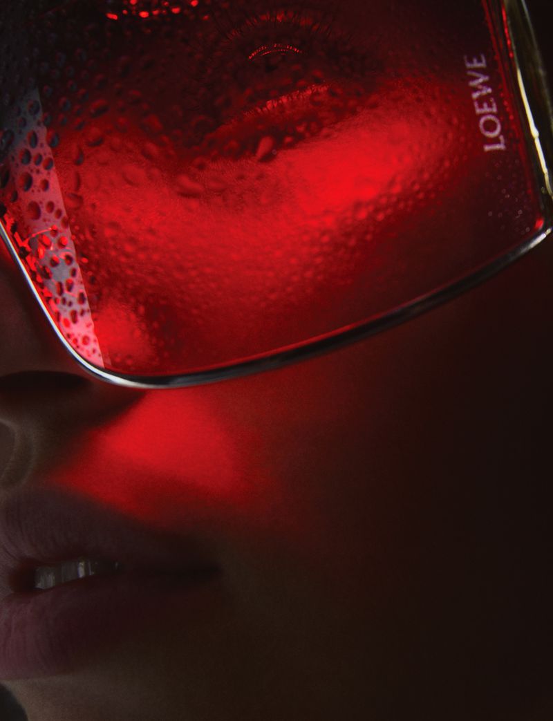 Close-up portrait of a person wearing tinted glasses with water droplets, illuminated by red light in a dark, indoor setting.
