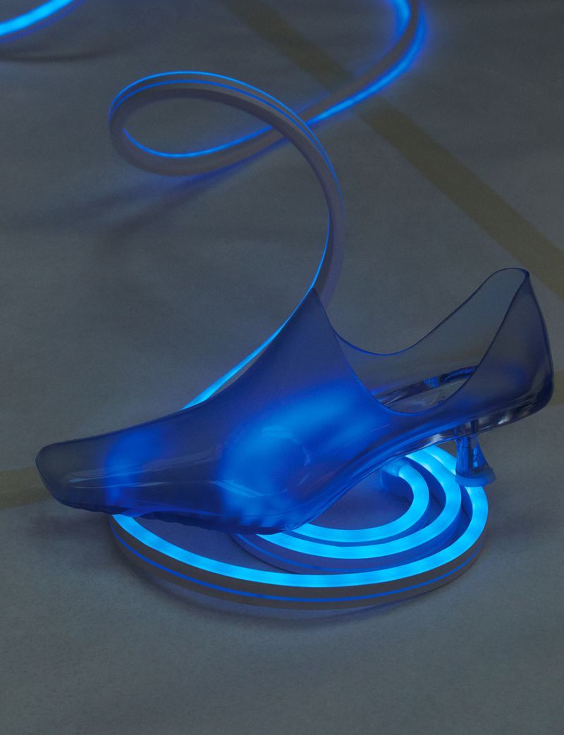 Transparent high-heel shoe illuminated in bright blue, set on a glowing white platform with a spiraling blue light behind it.