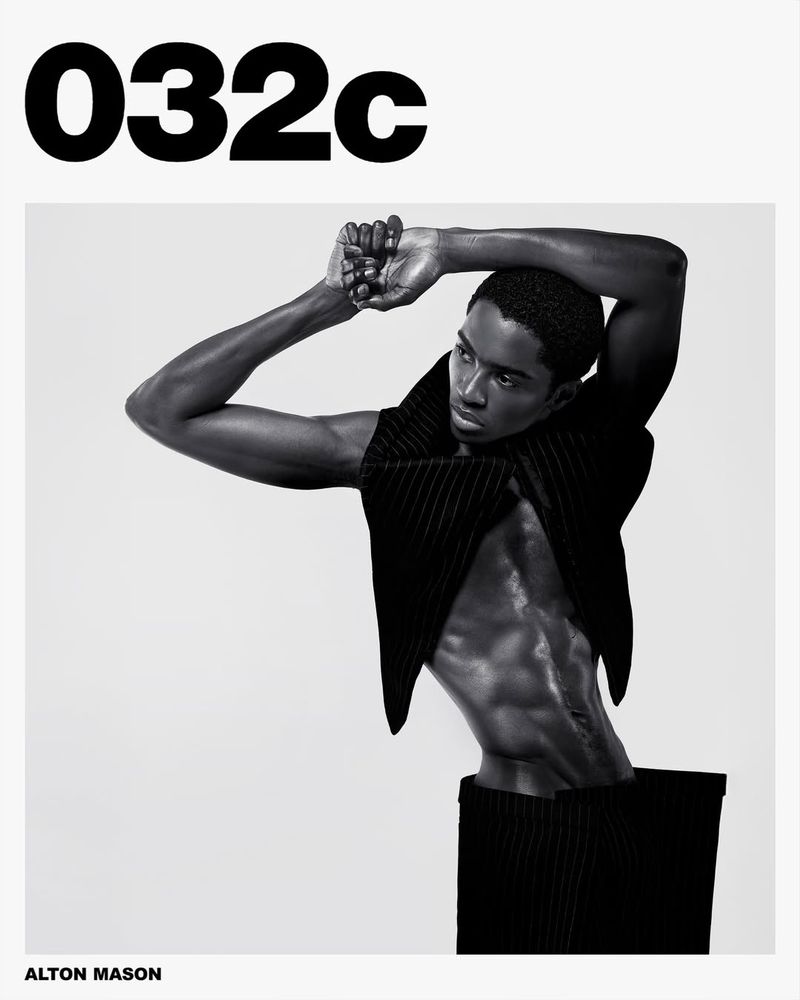 Black and white fashion portrait of an African American male model wearing a black vest and trousers against a plain grey backdrop.
