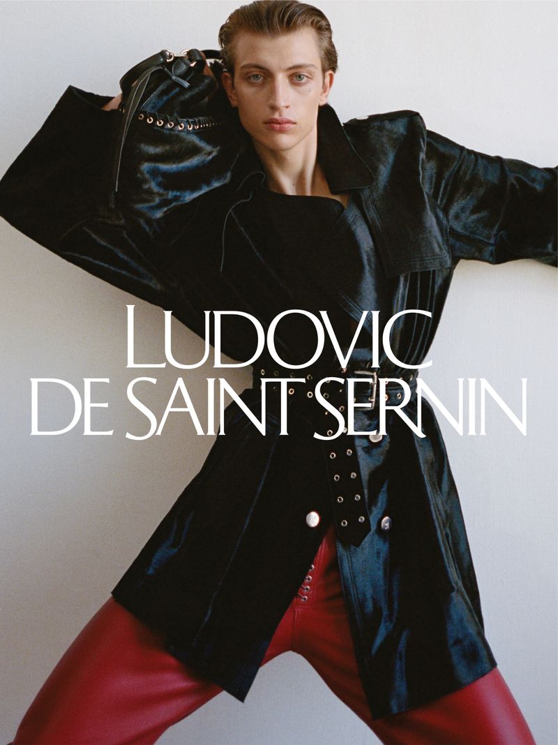 Male model posing in a black coat and red leather pants, captured indoors with white text overlay against a neutral background.