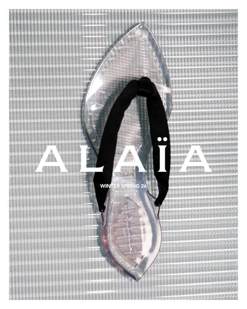 Clear sandal with black strap on gray striped background, ALAÏA Winter Spring 26 advertisement. Fashion footwear product shot.