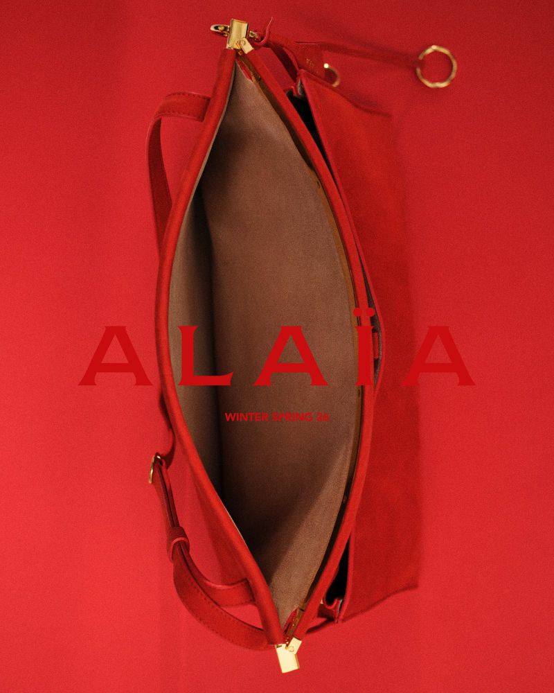Red leather shoulder bag with gold hardware and beige lining on a matching red backdrop, featuring the ALAÏA Winter Spring logo.