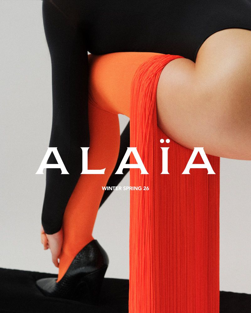 Fashion editorial featuring a woman in orange tights, black leotard, and heeled shoes, set against a soft grey background. Text overlay.