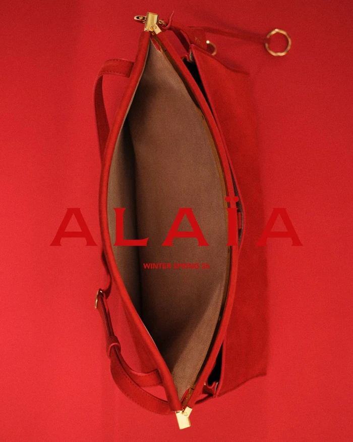 Overhead studio shot of a red leather handbag on a matching solid red background featuring the Alaia logo