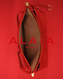 Overhead studio shot of a red leather handbag on a matching solid red background featuring the Alaia logo
