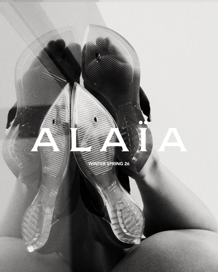 Low angle view showing the translucent soles of clear shoes worn upside down with Alaïa branding visible.