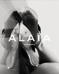 Low angle view showing the translucent soles of clear shoes worn upside down with Alaïa branding visible.