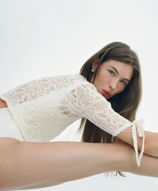 Woman posing in a white lace top in a close-up shot with a white background, showcasing fashion and beauty.