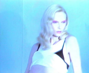 Blonde model with pink eyeshadow wearing white top against blue lit background for Acne Paper project.