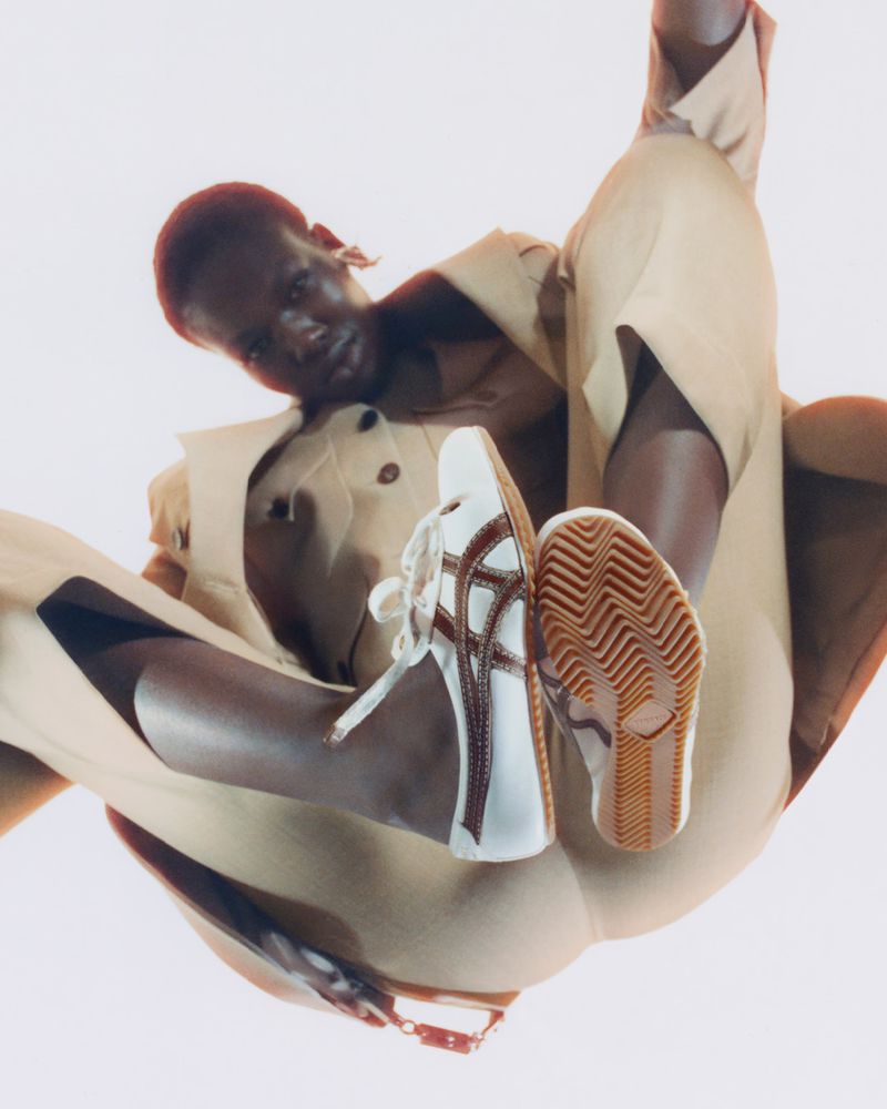 Person wearing tan clothing and white and brown athletic shoes posing in studio environment with a bright background.
