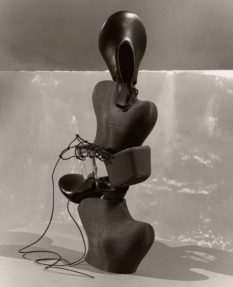 Abstract composition of dark-toned vintage shoe forms stacked vertically against a mottled light background in an indoor setting.