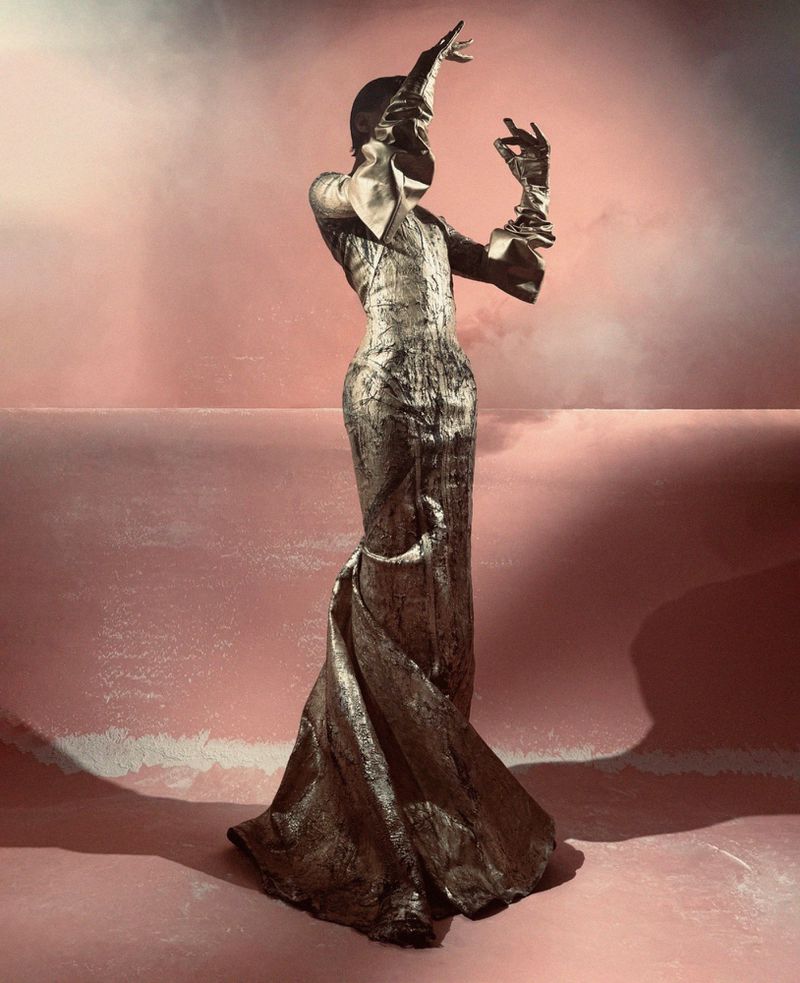 Fashion photography featuring a person wearing a bronze metallic gown and gloves in an artistic pose with a stylized background.